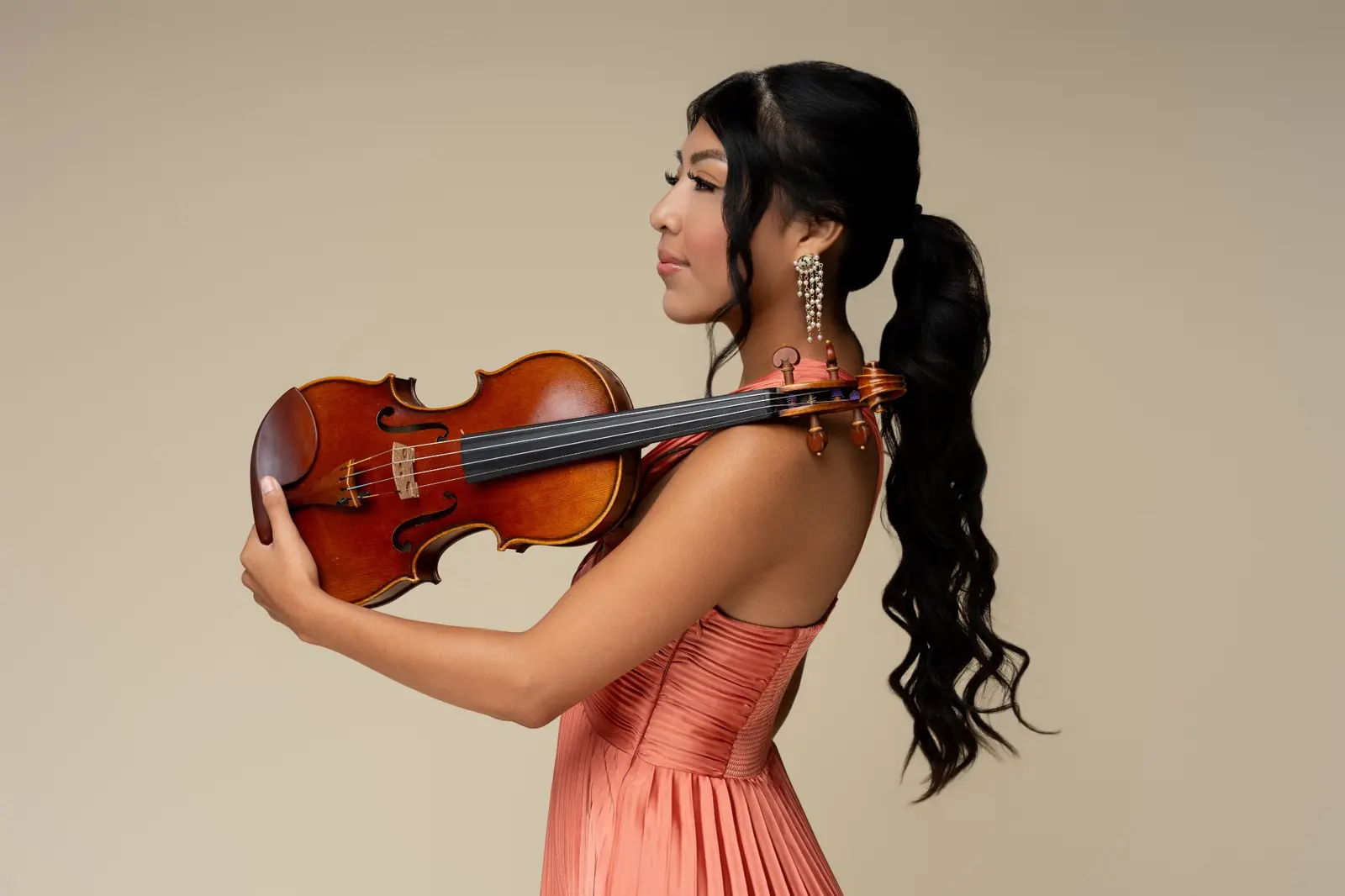 Bets holding her violin in an elegant coral gown